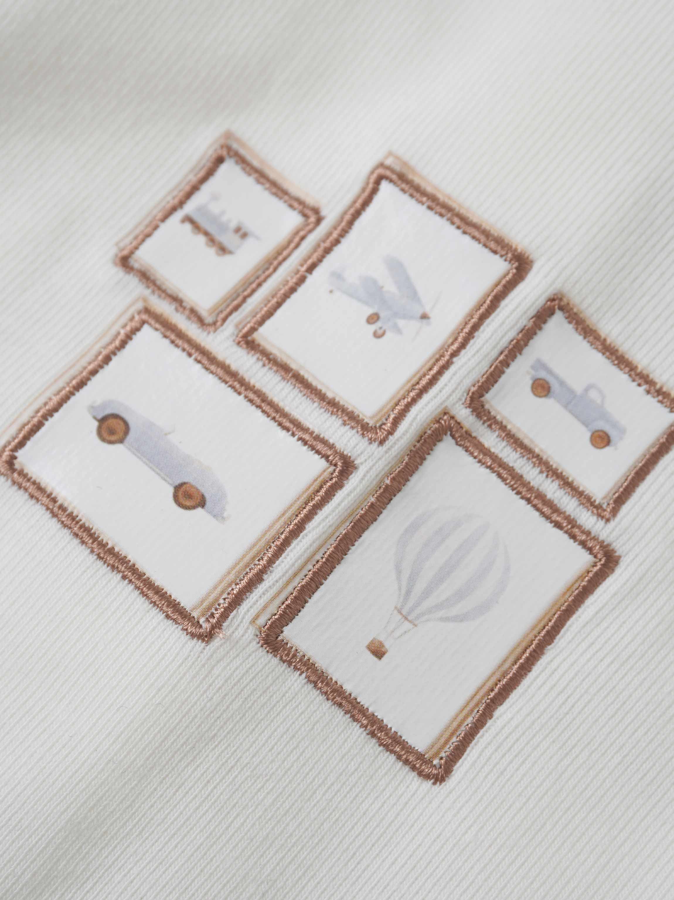 Adee Mini Gallery Stretchy boys jumpsuit; white fabric with brown-framed square patches showing toy illustrations.
