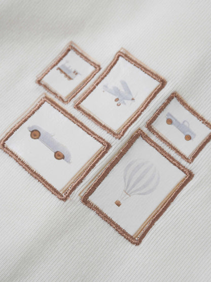 Adee Mini Gallery Stretchy boys jumpsuit; white fabric with brown-framed square patches showing toy illustrations.