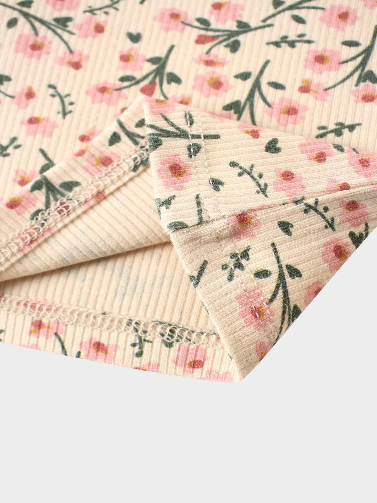 Floral print fabric in pink and green on light tan ribbed knit, folded short sleeve with pleated trim.