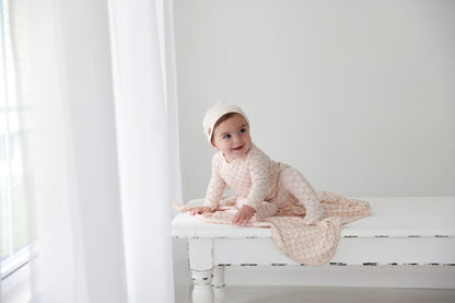 Floral Garland Stretchy girls stretchies by Adee in pale pink floral print worn by a baby girl on a white bench.