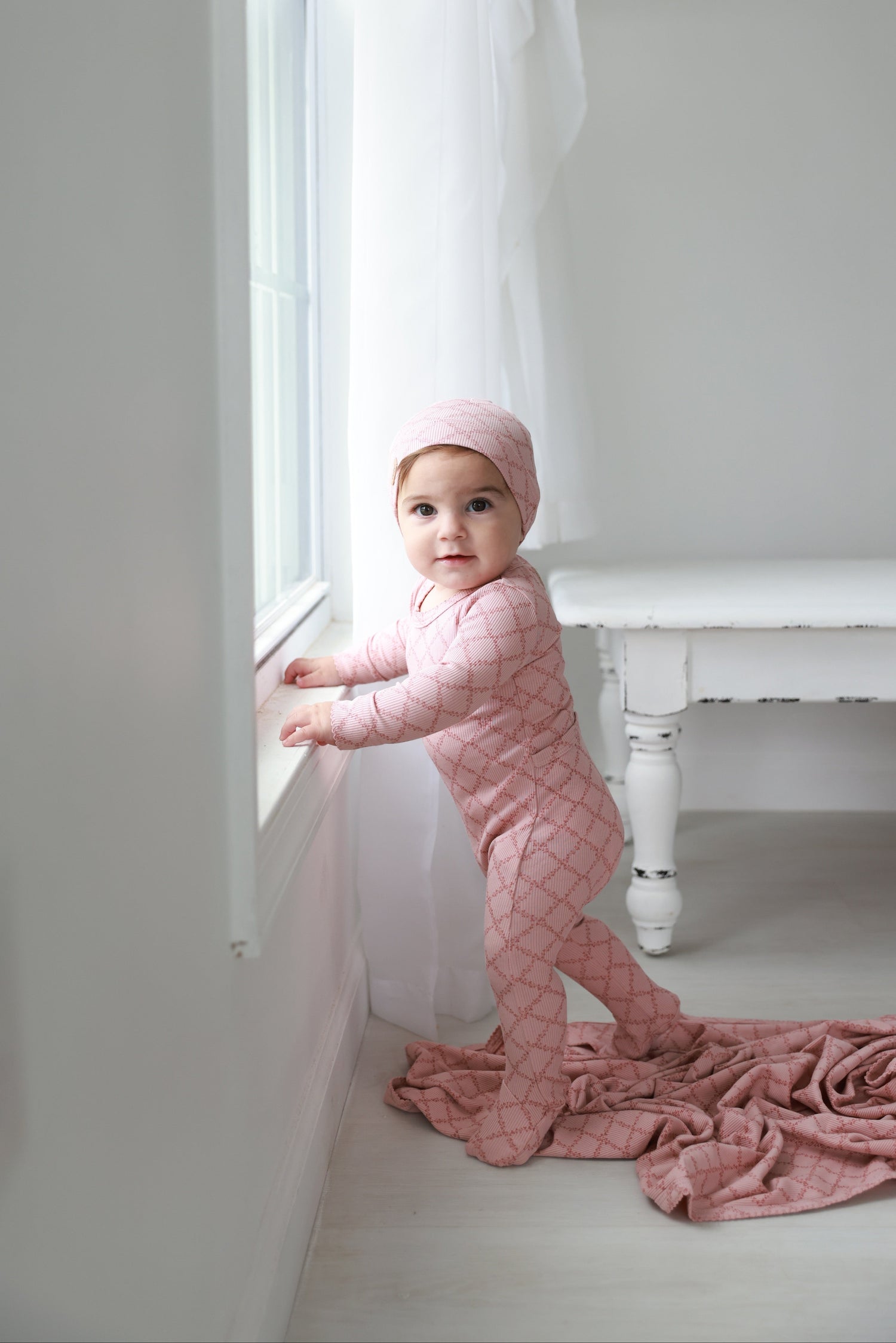 Pink Leaf layette set for girls in pink knit with diamond lattice pattern, baby by window wearing matching hat