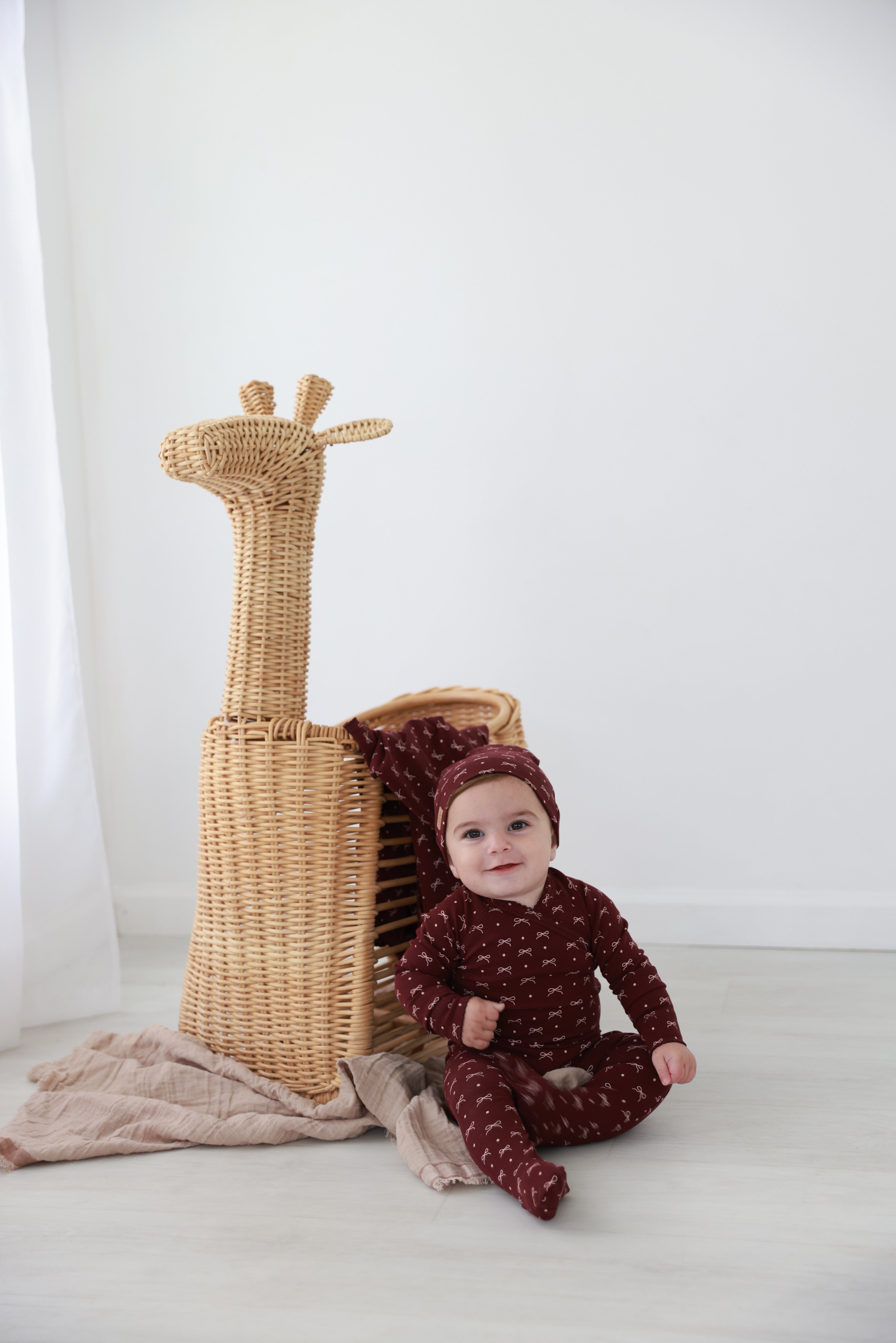 Burgundy Bow Stretchy girls stretchies by Adee; maroon fabric with small bow pattern, worn by baby.