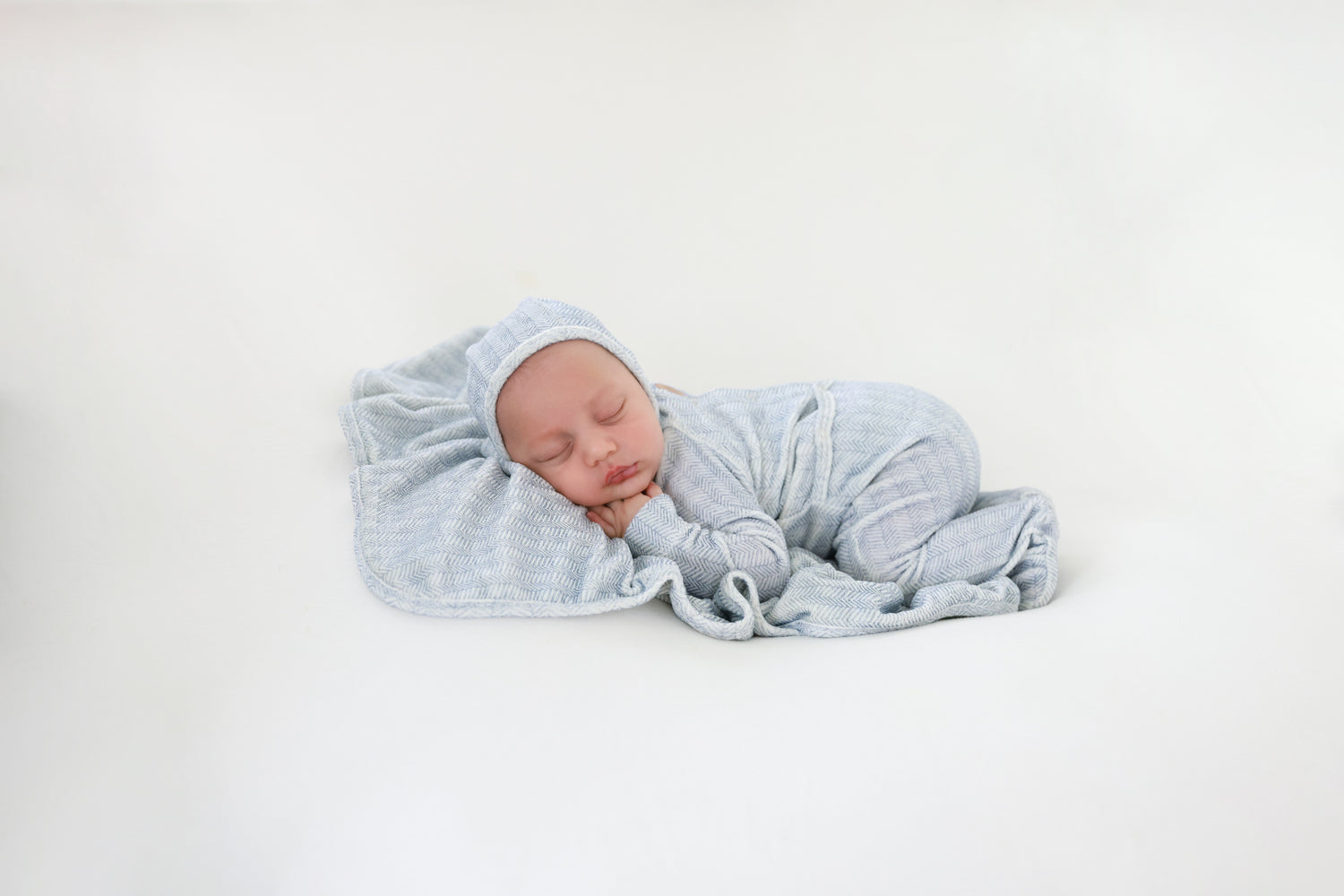 Heritage Herringbone Blue layette set, baby swaddled in blue herringbone fabric.