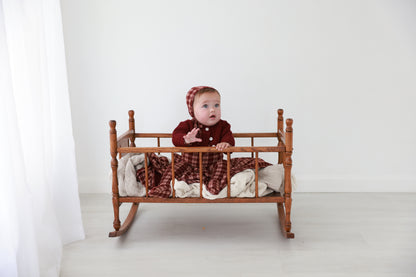 Burgundy plaid layette set for baby girls, includes matching hat, worn by a baby in a wooden crib.