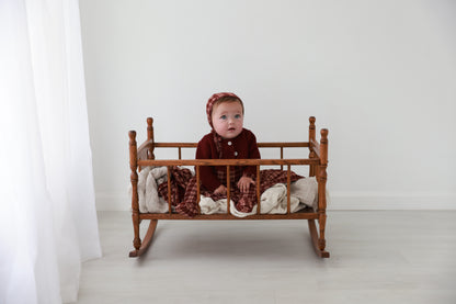 Girls Stretchies Burgundy Plaid outfit by Adee worn by a baby in a plaid bonnet in a wooden cradle