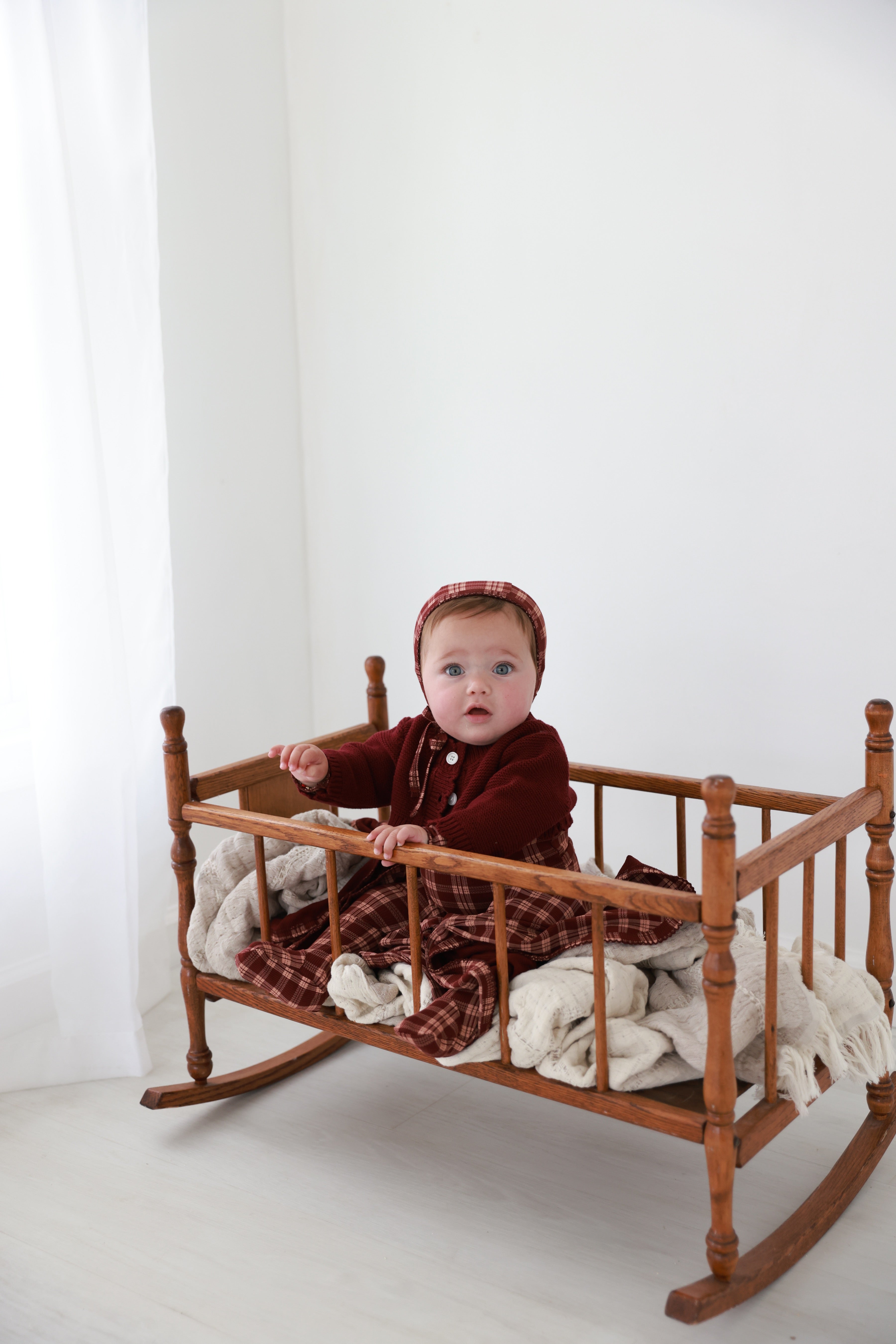 Cropped cardigan burgundy by Adee; unisex dressy top worn by baby in a wooden cradle