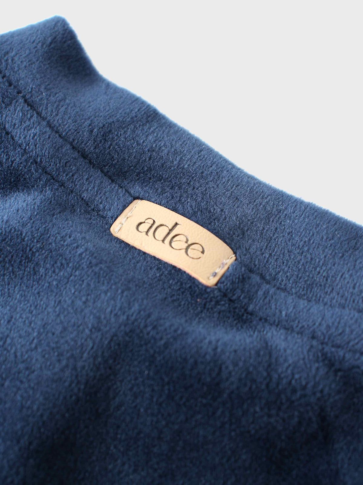 Navy velour bomber fabric close-up with beige label reading adee