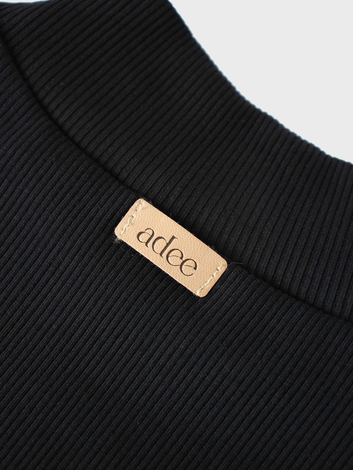 Close-up of black ribbed mock-neck shirt fabric with beige adee brand tag.