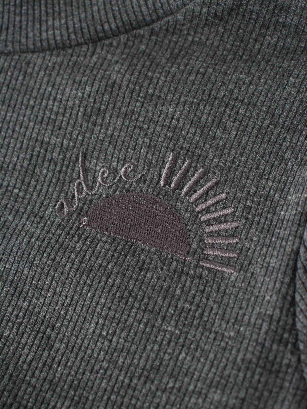 Grey ribbed knit fabric with embroidered sunburst design on puff-sleeve shirt detail.