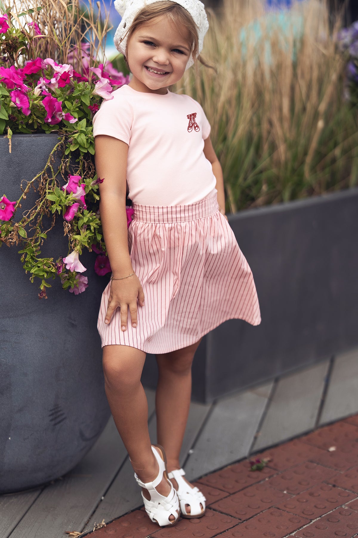 Striped pink and white cotton skirt for girls by Adee, shown on a smiling child outdoors.