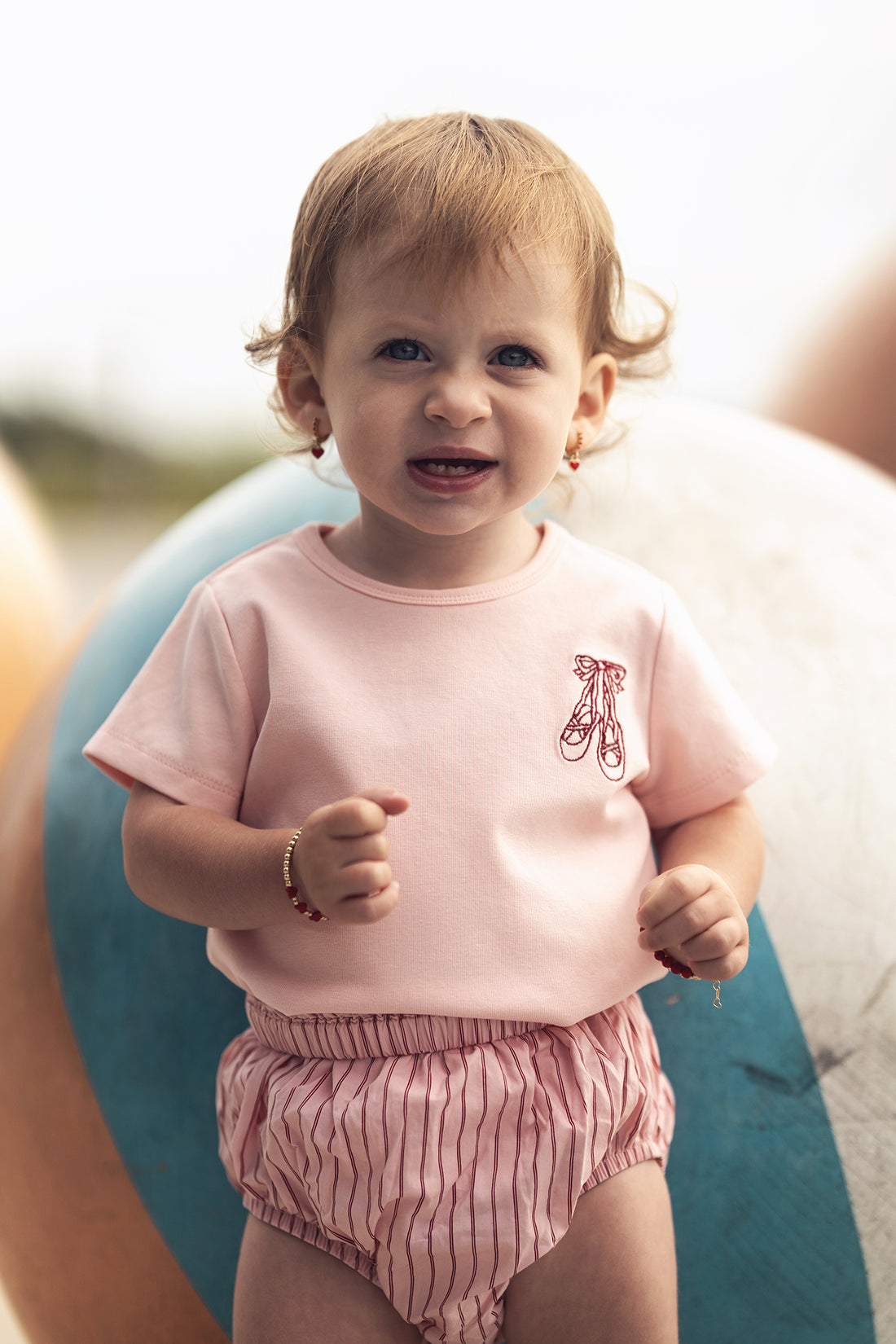 Toddler wearing pink striped cotton bloomers with a matching pink top, outdoors.