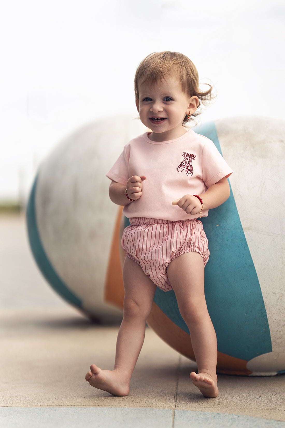 Toddler girl wearing Striped Cotton Bloomers - Pink, outdoors, smiling.