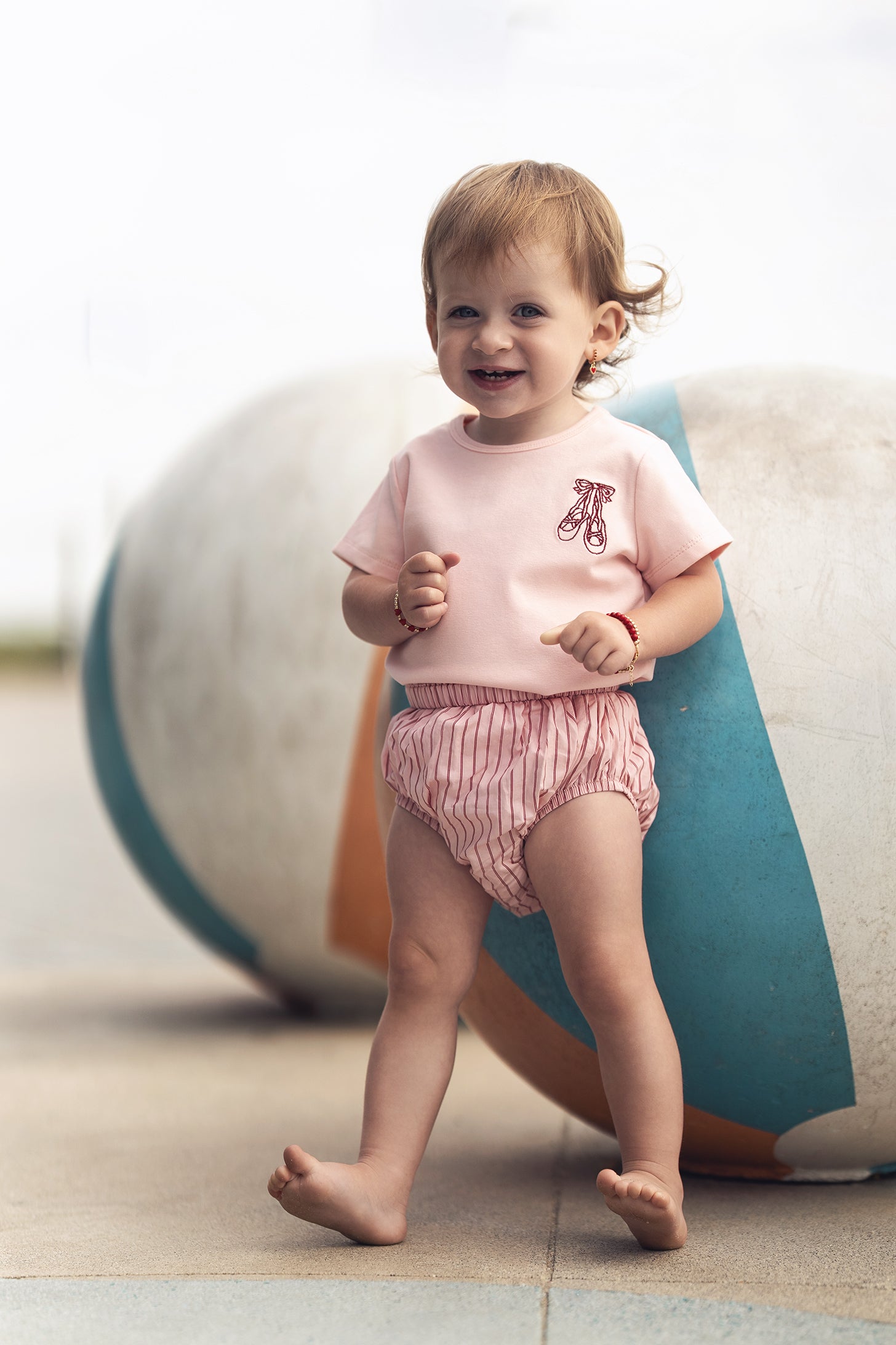 Toddler girl wearing Striped Cotton Bloomers - Pink, outdoors, smiling.