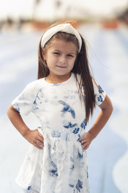 Young girl wearing a white short-sleeve dress with blue floral print and a white headband.