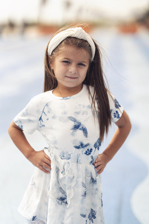 Young girl wearing a white short-sleeve dress with blue floral print and a white headband.
