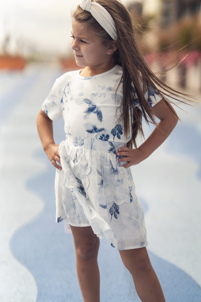 Girl wearing a blue flower print short-sleeve top with a light skirt, outdoors with a headband.