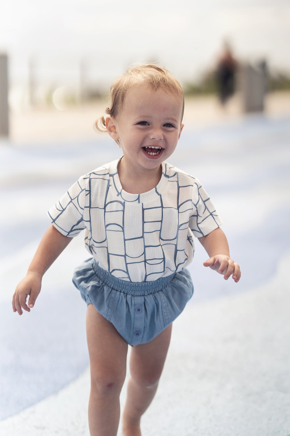 Abstract T-shirt on a smiling toddler in a light-beige top with a light-blue geometric pattern and blue shorts.