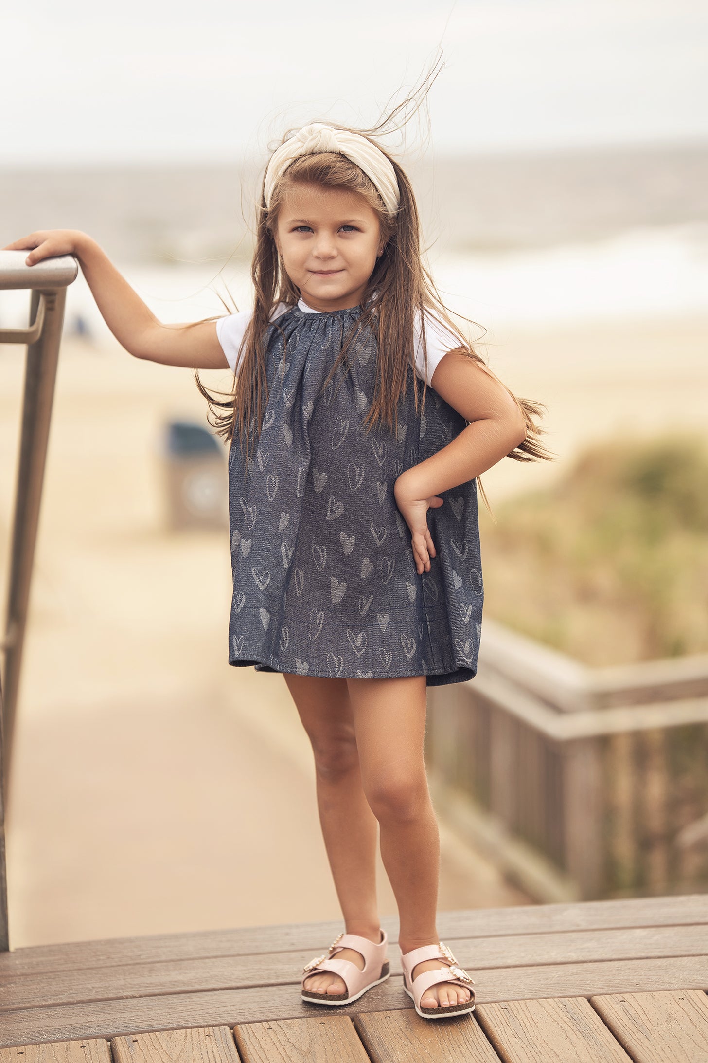 Girl in denim heart jumper posing on a beach boardwalk.