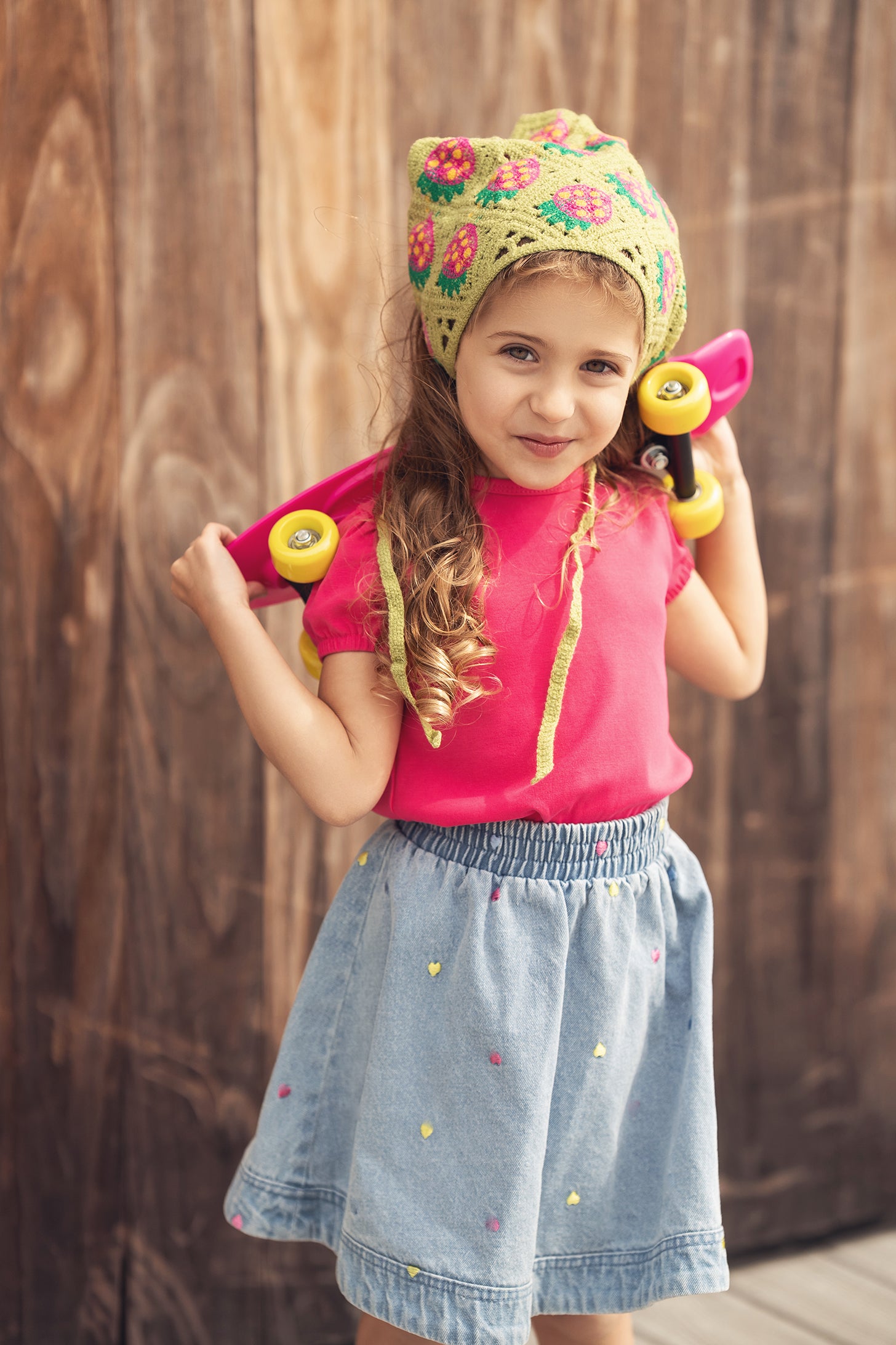 Little girl in pink top wearing Embroidered Heart Denim Skirt with tiny hearts, posing with a pink skateboard.