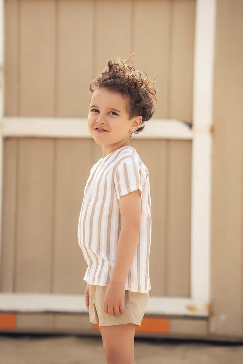 Young child in tan cotton shorts and a light striped shirt, outdoors, side profile.