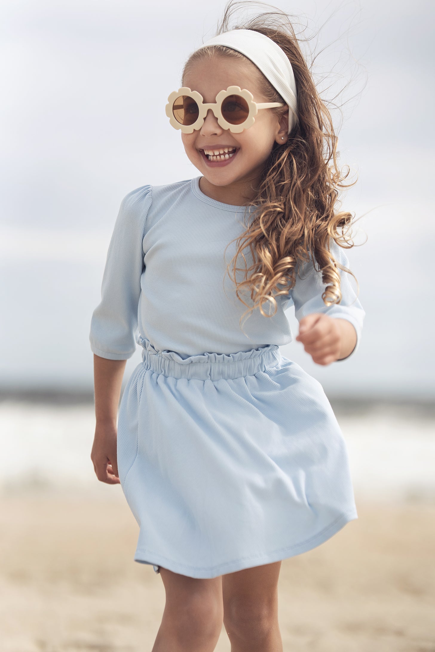 Smiling girl in a light blue 3/4 puff sleeve T-shirt at the beach.