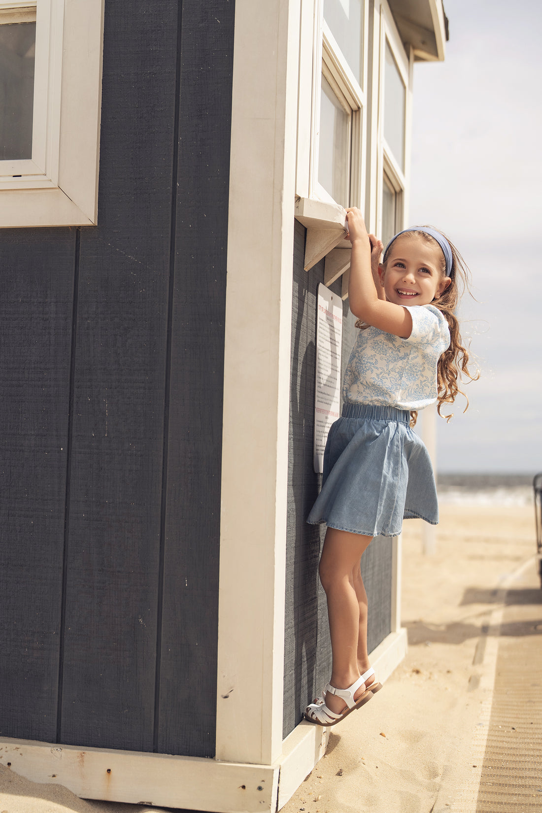 Smiling girl wearing a blue flowered short-sleeve T-shirt at a beachside shack.