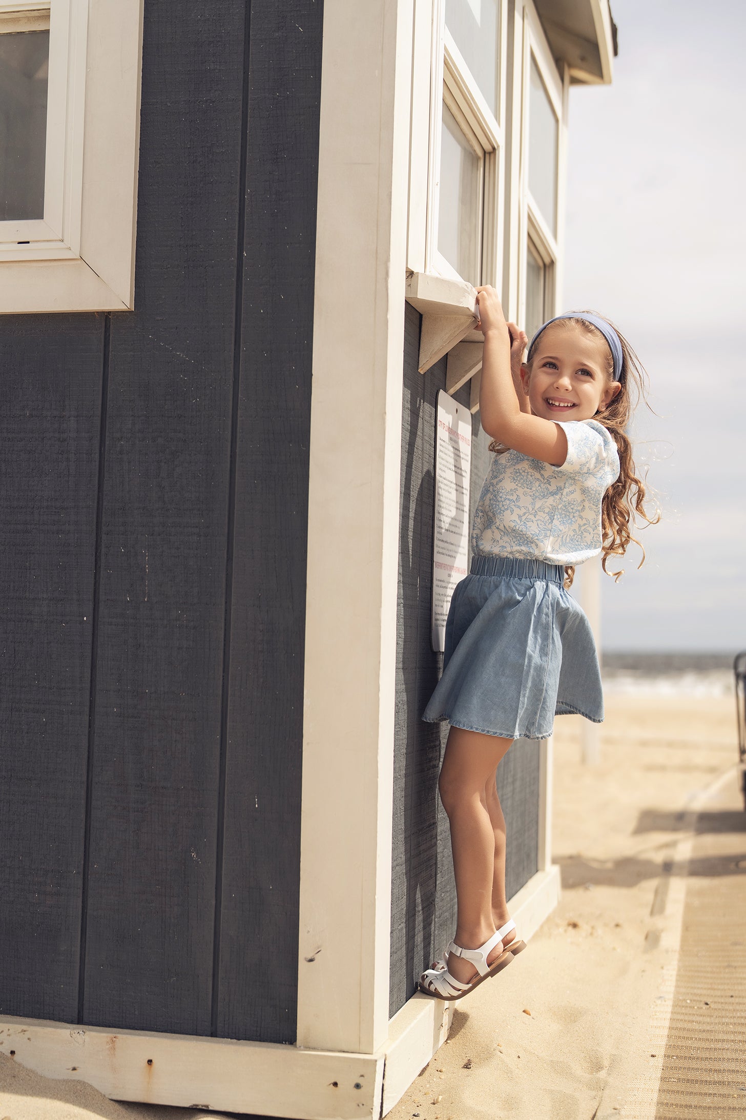 Smiling girl wearing a blue flowered short-sleeve T-shirt at a beachside shack.