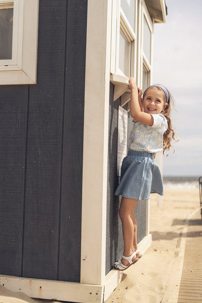 Smiling girl wearing a blue flowered short-sleeve T-shirt at a beachside shack.