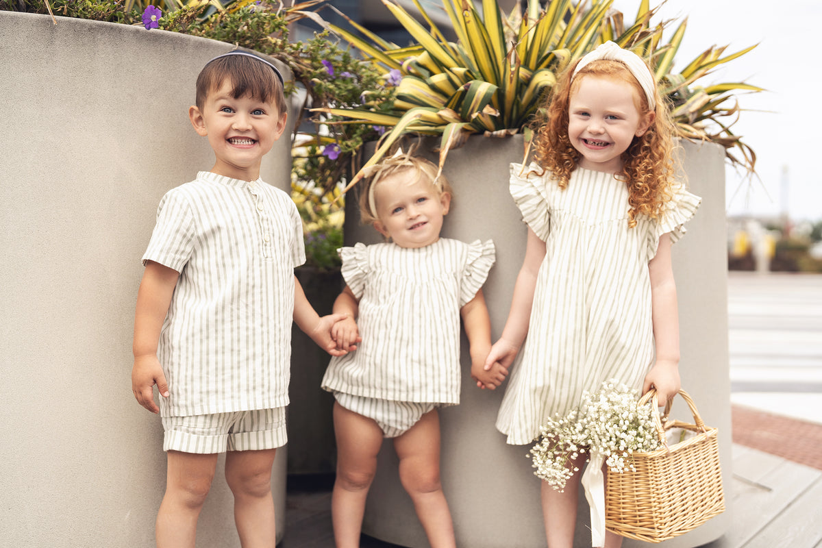 Green striped ruffled shirt and bloomers set by Adee for little girls, worn by three children outdoors