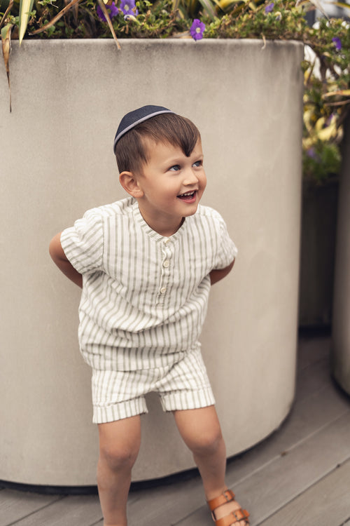 Smiling toddler in a green striped shirt and brown sandals outdoors.