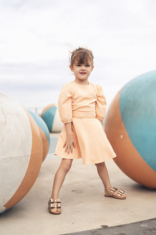 Peach 3/4 puff-sleeve dress on a young girl outdoors among oversized pastel spheres.
