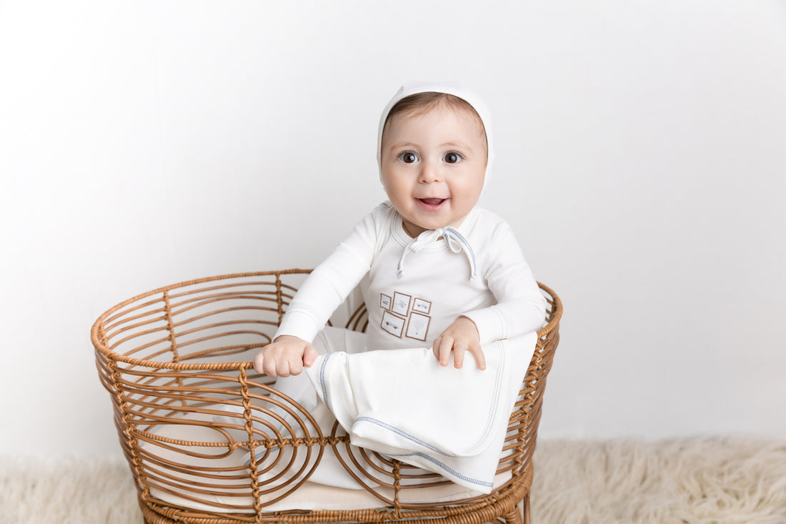 Mini Gallery Stretchy - Blue, white baby jumpsuit with light blue trim in a wicker basket.