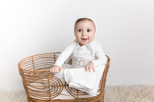 Mini Gallery Stretchy - Blue, white baby jumpsuit with light blue trim in a wicker basket.