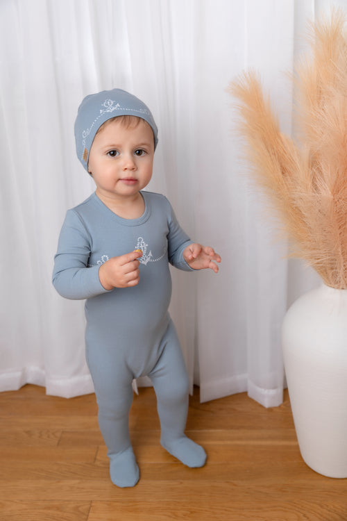 Blue Anchor Stretchy: light-blue baby jumpsuit footie with white rope loops and central anchor, worn with matching hat.